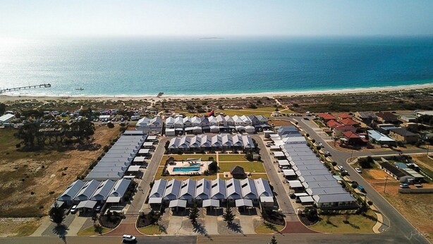 An aerial view of a coastal resort with multiple bungalow-style accommodations, a central pool, and a beach in the background. - Unit 64 Seafront Estate (Jurien Bay)