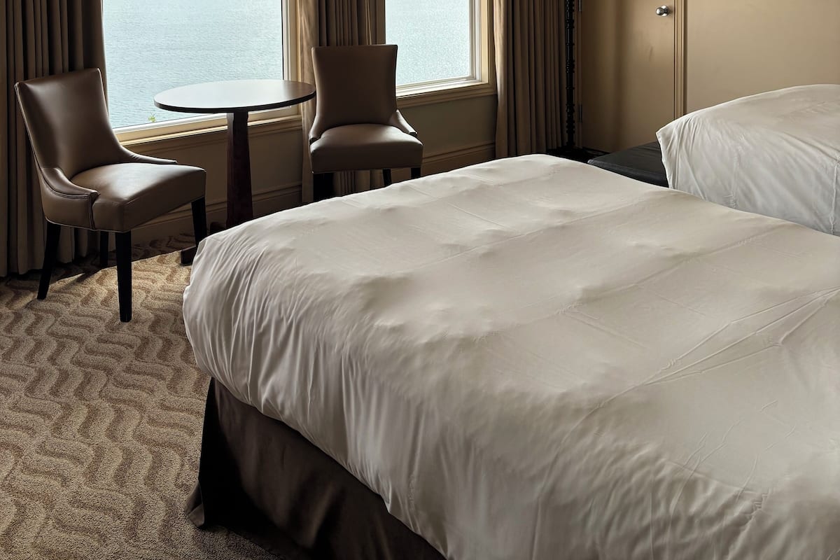 A hotel room with two beds, a chair, a small table, and a view of a body of water.