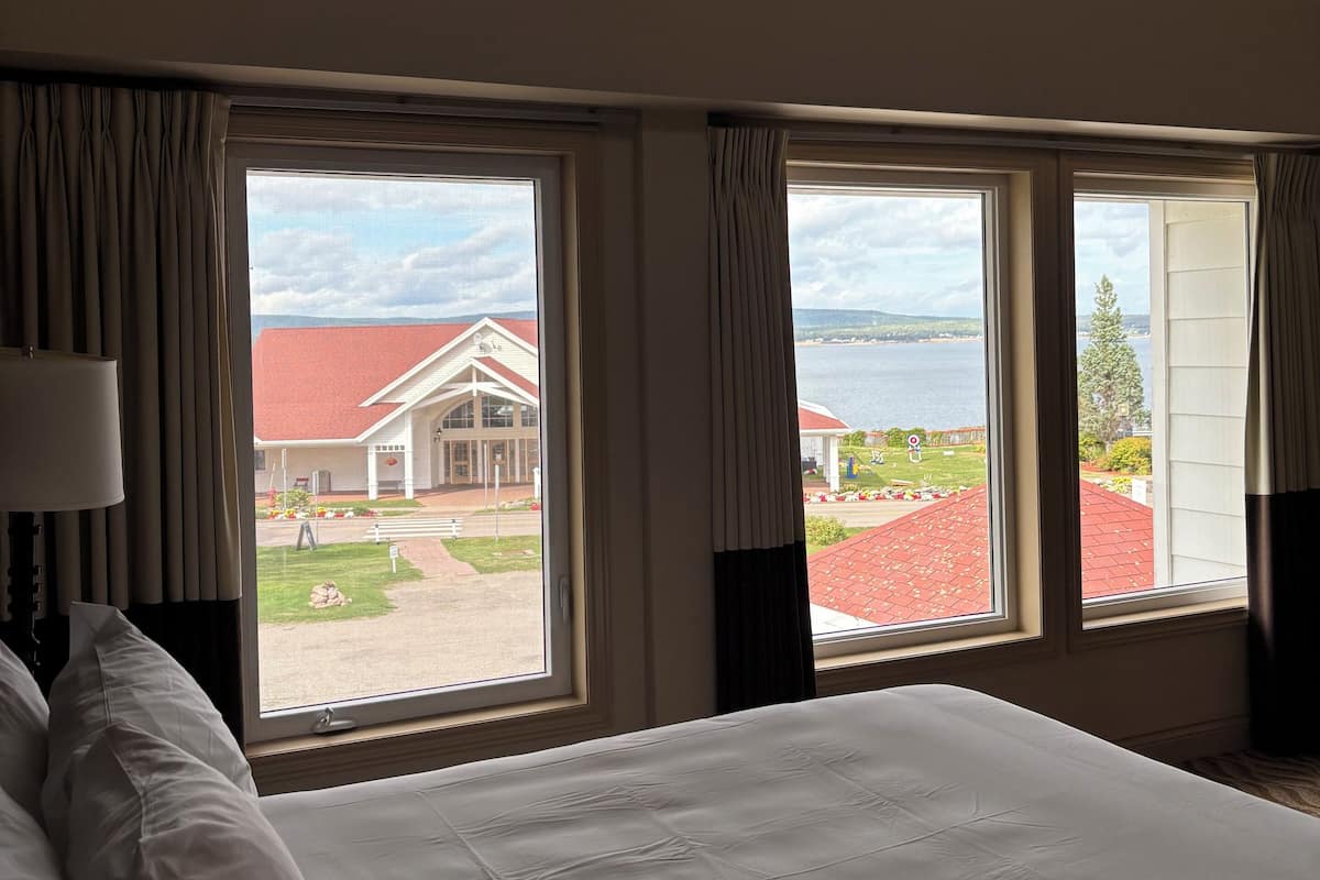 A hotel room with a large bed, two windows with curtains, and a view of a building and water.