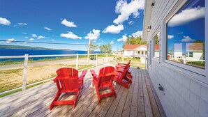 Une terrasse en bois avec des fauteuils Adirondack rouges donnant sur une plage et l’océan.