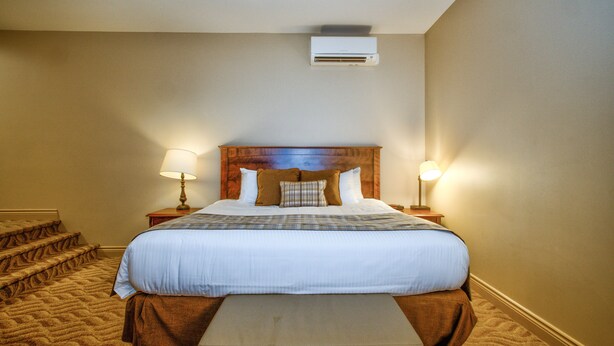 Une chambre d’hôtel avec un grand lit, deux lampes de chevet, une tête de lit en bois, un banc au pied du lit et un sol recouvert de moquette.