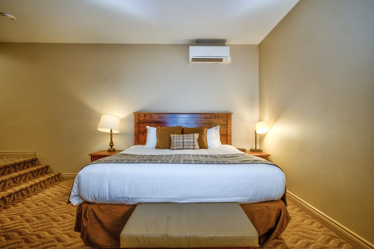 A hotel room with a large bed, two bedside lamps, a wooden headboard, a bench at the foot of the bed, and a carpeted floor.