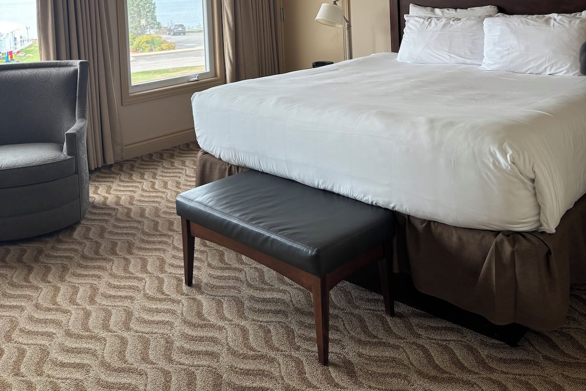 A hotel room with a large bed, a bench, a chair, a nightstand, and a view of the outdoors.