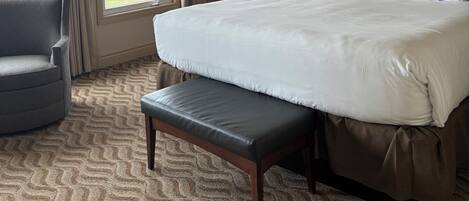 A hotel room with a large bed, a bench, a chair, a nightstand, and a view of the outdoors.