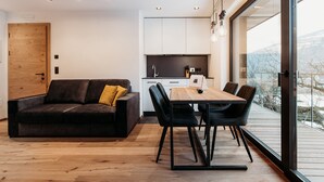 A modern living room with a wooden floor, a dark brown sofa with a yellow pillow, a wooden dining table with four chairs, and a kitchen area with white cabinets and a black countertop. - Modern-traditional apartment with a great view (Albeins)