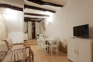 Un salon doté d’un téléviseur, de meubles blancs et de poutres apparentes.