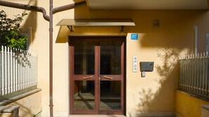 Une entrée d’immeuble avec une porte en verre, un portail en métal et un sol pavé de carreaux.