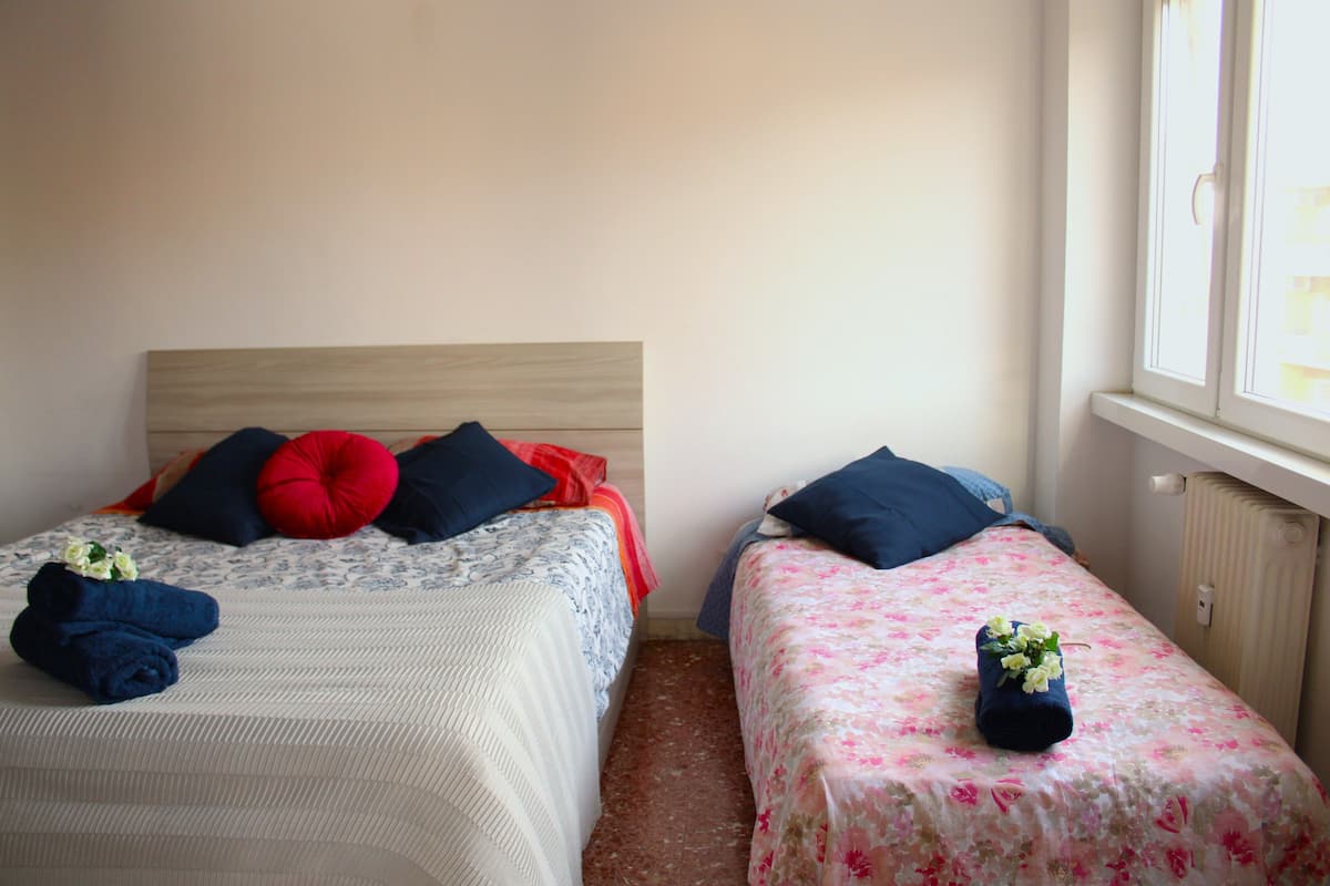 Zwei Einzelbetten mit unterschiedlicher Bettwäsche, eine Heizung und ein Fenster mit Jalousien.