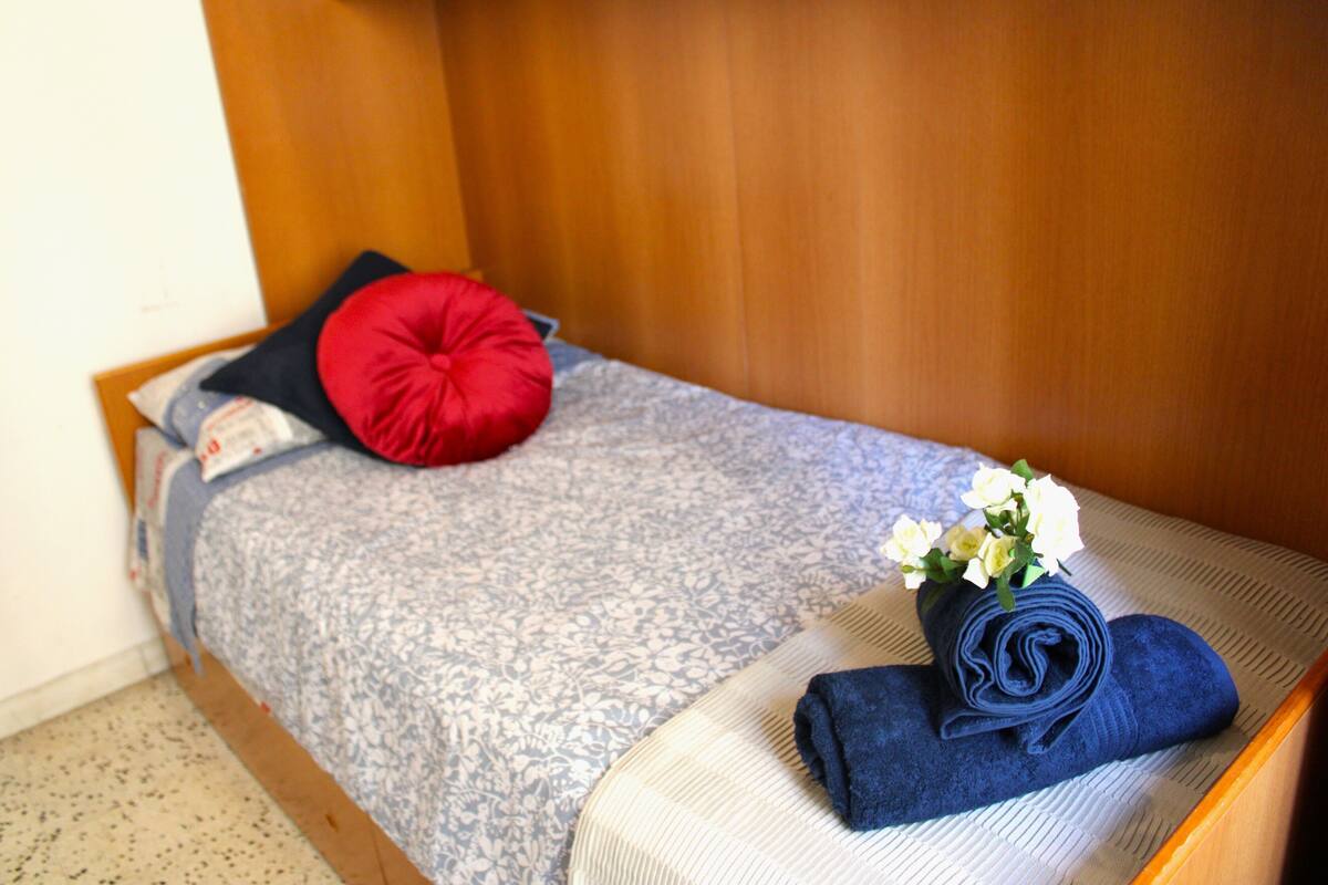 Ein ordentlich bezogenes Bett mit einer Blumenkomposition und einem aufgerollten Handtuch.