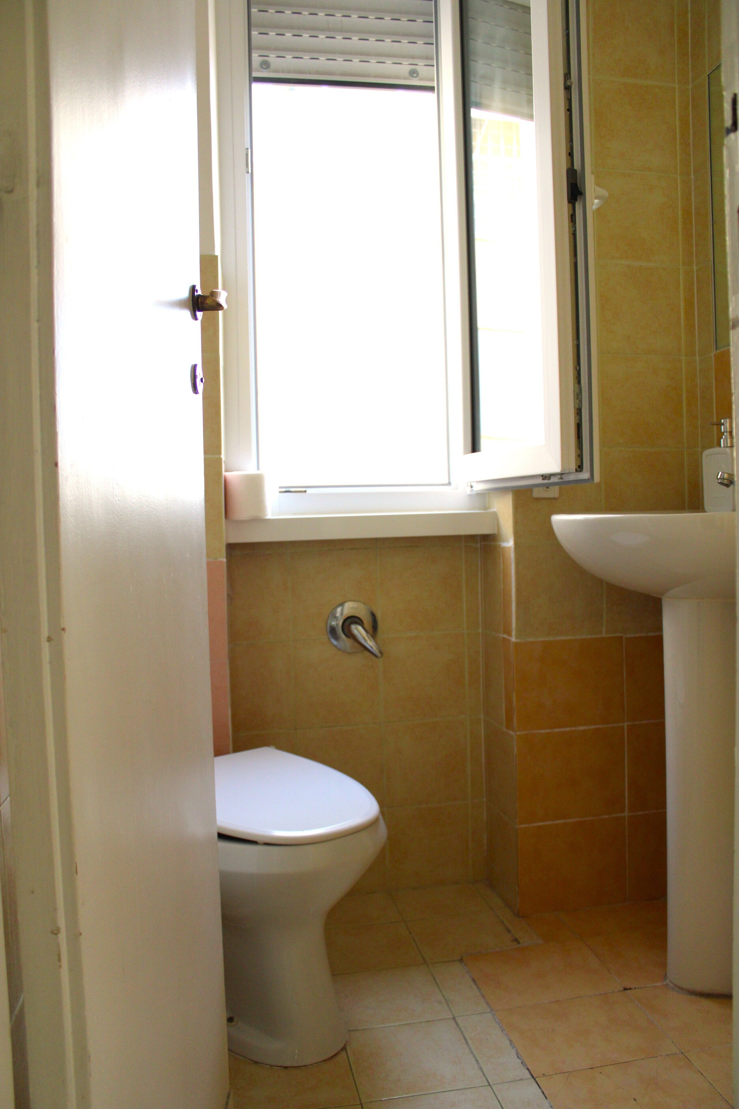 A small bathroom with a toilet, a window, and a sink.