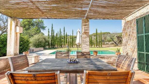 An outdoor patio with a table and chairs, a pool, and a view of trees and hills. - Son Viverassa, Finca 5StarsHome Mallorca (Son Servera)