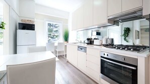 A modern kitchen with white cabinetry, a built-in oven, and a dining area with a white table and chairs. - Snug 1-Bed Unit Across from Bondi Beach (Bondi Beach)