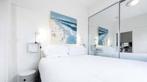 A modern hotel room with a large bed, a bedside table, a small trash bin, and a large mirror reflecting the room. - Snug 1-Bed Unit Across from Bondi Beach (Bondi Beach)