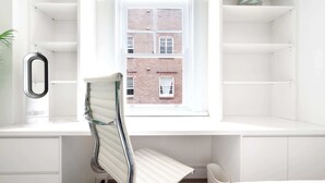 A modern, minimalist room with a built-in desk, a chair, and a window overlooking a brick building. - Snug 1-Bed Unit Across from Bondi Beach (Bondi Beach)