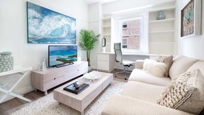 A modern living room with a large TV, a sofa, a coffee table, and a bookshelf. - Snug 1-Bed Unit Across from Bondi Beach (Bondi Beach)