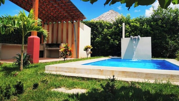 A swimming pool with a waterfall feature, surrounded by lush greenery and a pergola structure. - Private house with pool, near Tamarindo. (Provincia de Guanacaste)