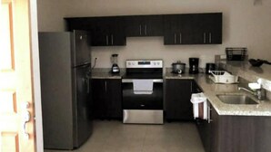 A compact kitchen with dark cabinets, a stainless steel refrigerator, a built-in oven, a coffee maker, and a sink. - Private house with pool, near Tamarindo. (Provincia de Guanacaste)
