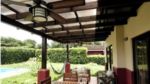 A covered outdoor seating area with a wooden table and chairs, a hammock, and a pool in the background. - Private house with pool, near Tamarindo. (Provincia de Guanacaste)