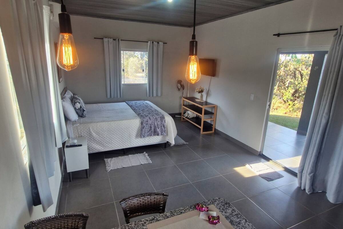 Ein Schlafzimmer mit Bett, Nachttisch, Lampe und Blick ins Freie.