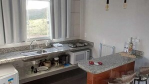 Una cocina con encimera de granito, lavaplatos integrado, refrigerador y una barra con taburetes.