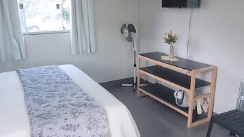 A bedroom with a bed, a TV mounted on the wall, a wooden side table, and a window with curtains.