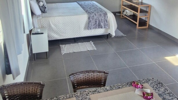 Een slaapkamer met een bed, nachtkastjes, een raam met gordijnen, een ventilator aan de muur en een klein houten plankje.