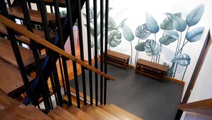 A wooden staircase with black railings and a view of a room with wooden benches and large decorative leaves on the wall. - Nara Residence Trang (Trang)