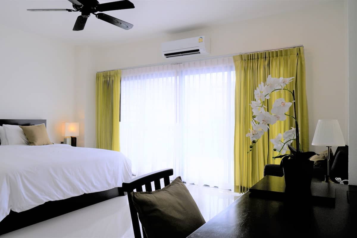 Una habitación de hotel con cama, escritorio, silla, lámpara, aire acondicionado y ventilador de techo.