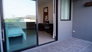 Une chambre moderne avec une porte vitrée donnant sur un balcon, un lit, un bureau et un miroir.