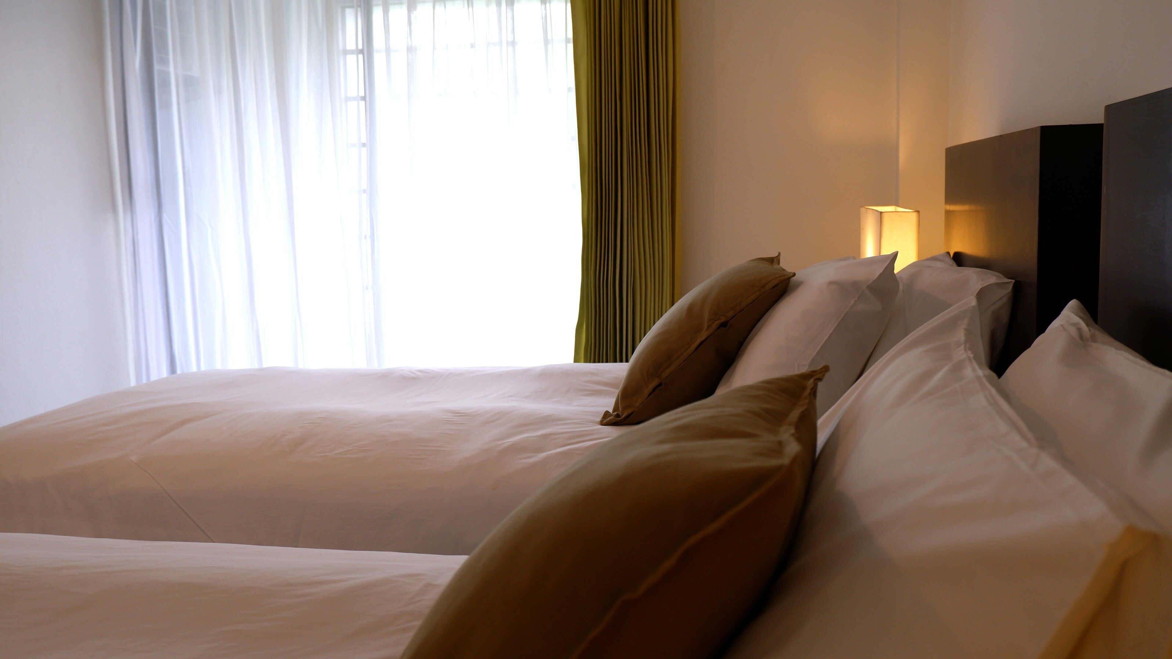 Una habitación de hotel con una cama grande, un cabecero con una lámpara y cortinas translúcidas.