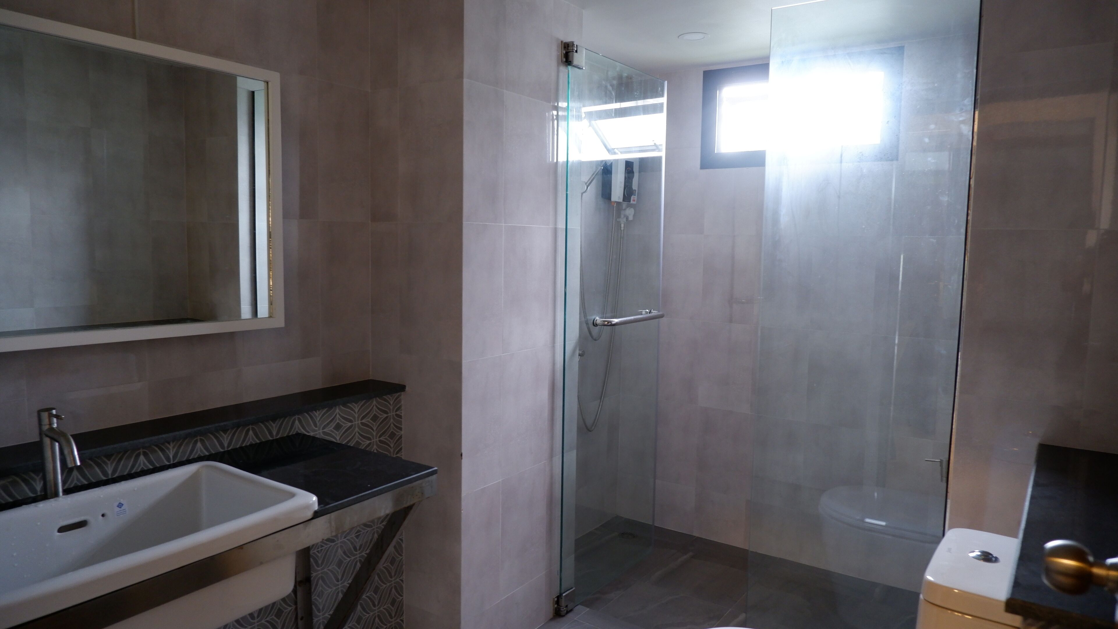 Een moderne badkamer met een douchecabine van glas, een wastafel met een zwart aanrechtblad en een toilet.