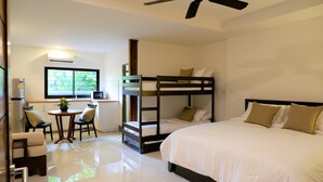 A room with bunk beds, a small table with chairs, a microwave, and a window with a view of greenery. - Nara Residence Trang (Trang)