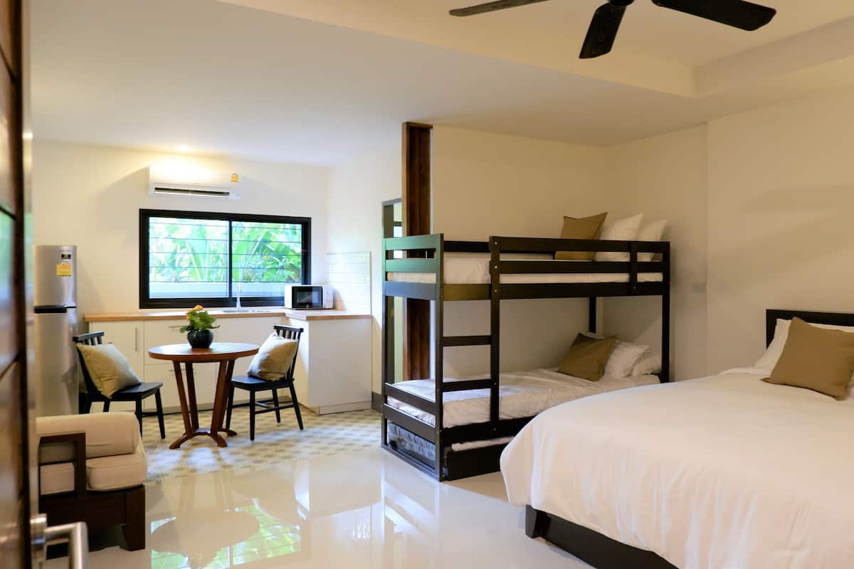 Una habitación con literas, una pequeña mesa con sillas, un microondas y una ventana con vistas a zonas verdes.