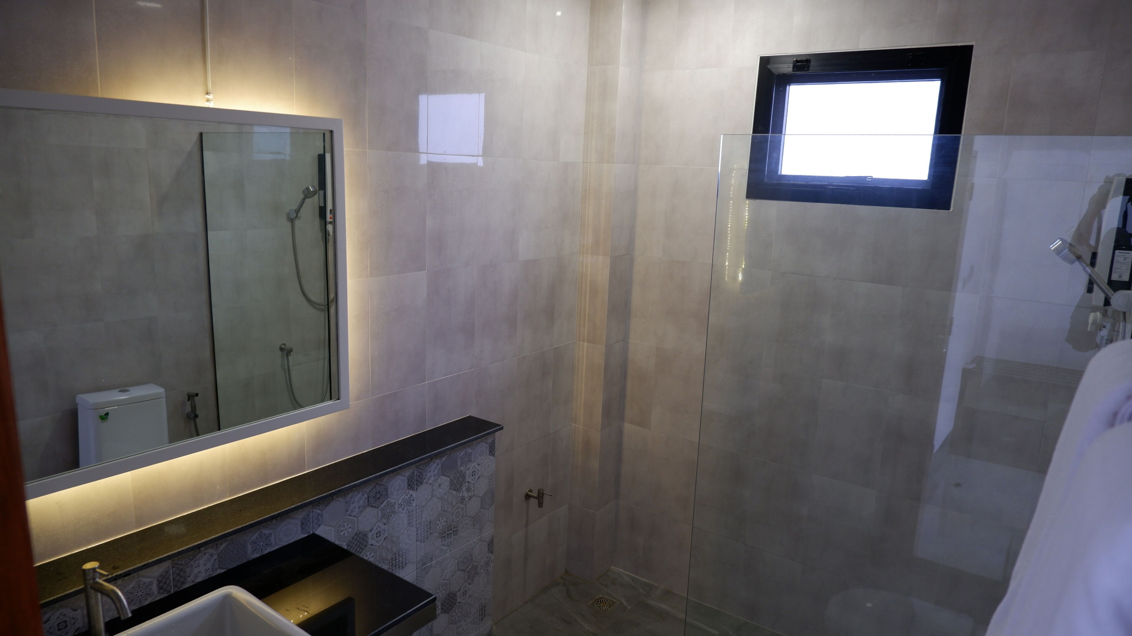 Un baño moderno con ducha de vidrio, un espejo grande y una ventana pequeña.