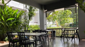 A covered outdoor seating area with tables and chairs, surrounded by potted plants and a view of greenery. - Nara Residence Trang (Trang)