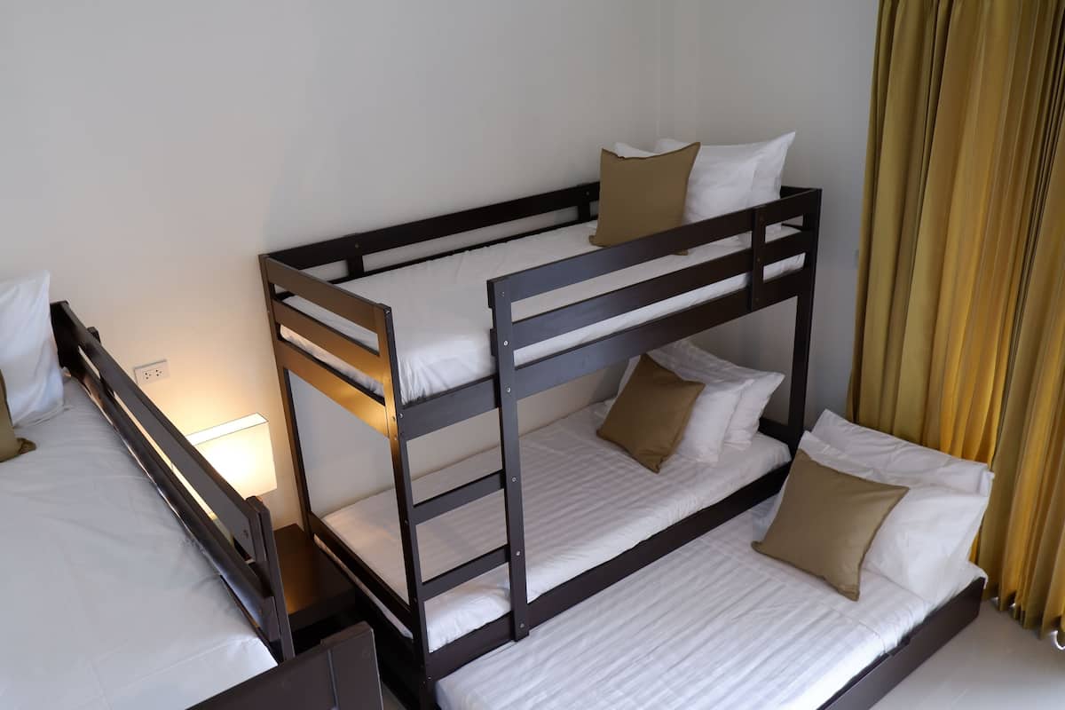 Habitación con literas, dos camas con ropa blanca y almohadas marrones. Una mesita de noche con lámpara junto a una de las camas.