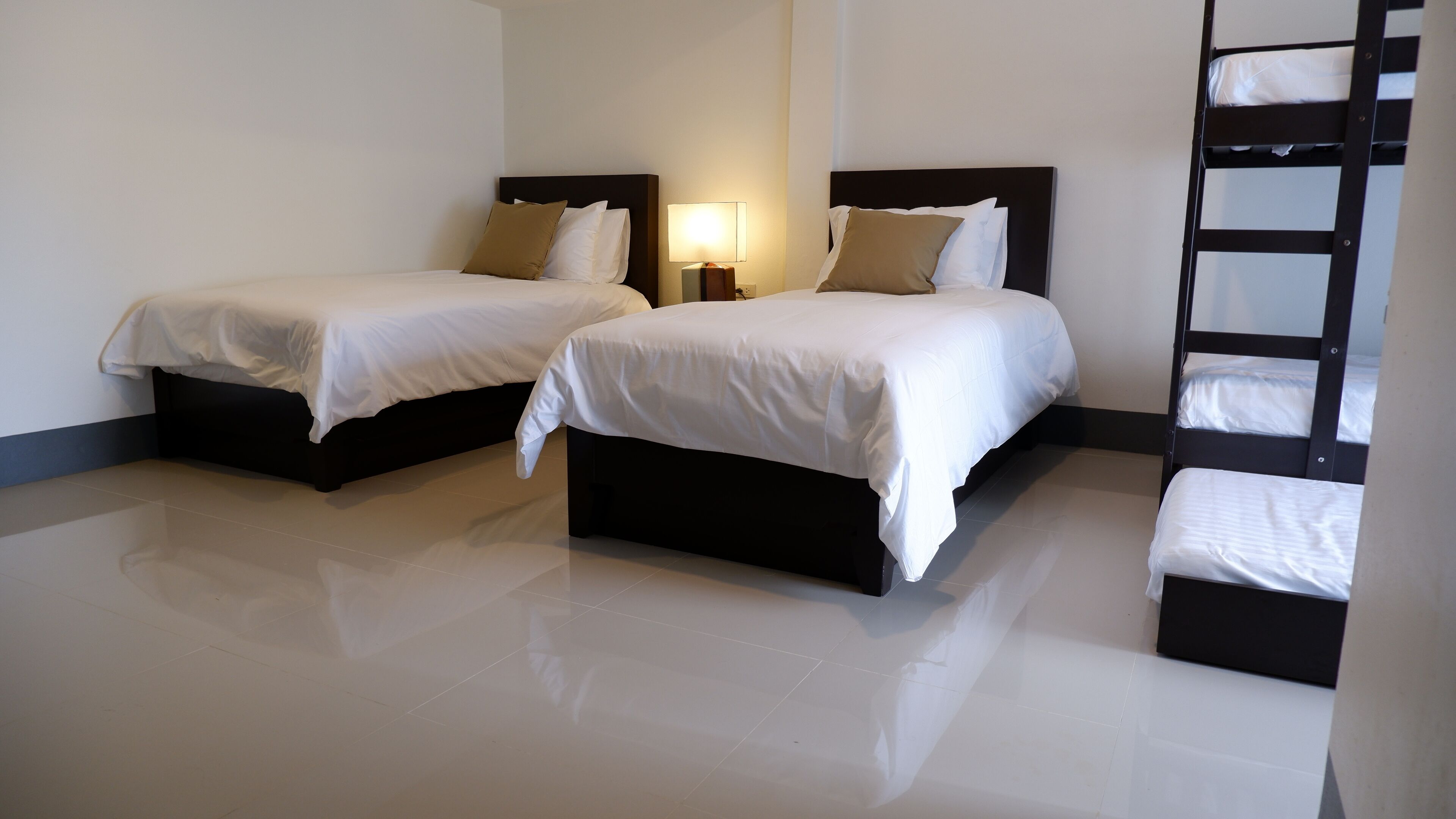A hotel room with two beds, a nightstand with a lamp, and a bunk bed.
