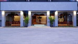 A hotel entrance with a modern design, featuring a central staircase leading to the lobby, flanked by two large potted plants and illuminated by warm lighting. - Nara Residence Trang (Trang)