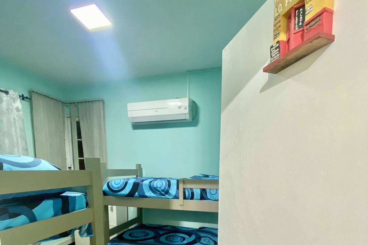 Una habitació amb lliteres, un aparell d'aire condicionat, una porta i un cartell penjat a la paret.