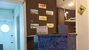 Un comptoir d’accueil avec un plateau en marbre, entouré d’un mur sombre orné de divers autocollants et d’une enseigne sur laquelle on peut lire : « VIVA CHILE ! ».