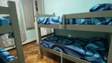 Habitación con literas, colchón estampado, suelo de madera y un equipo de aire acondicionado en la pared.