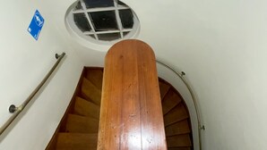 Un escalier en bois avec une rampe, une petite fenêtre et une enseigne bleue sur le mur.