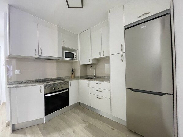 A modern kitchen with white cabinets, a stainless steel refrigerator, a microwave, a stove, and a sink. - MODERN STYLE CABALLOS (R140) (Benidorm)