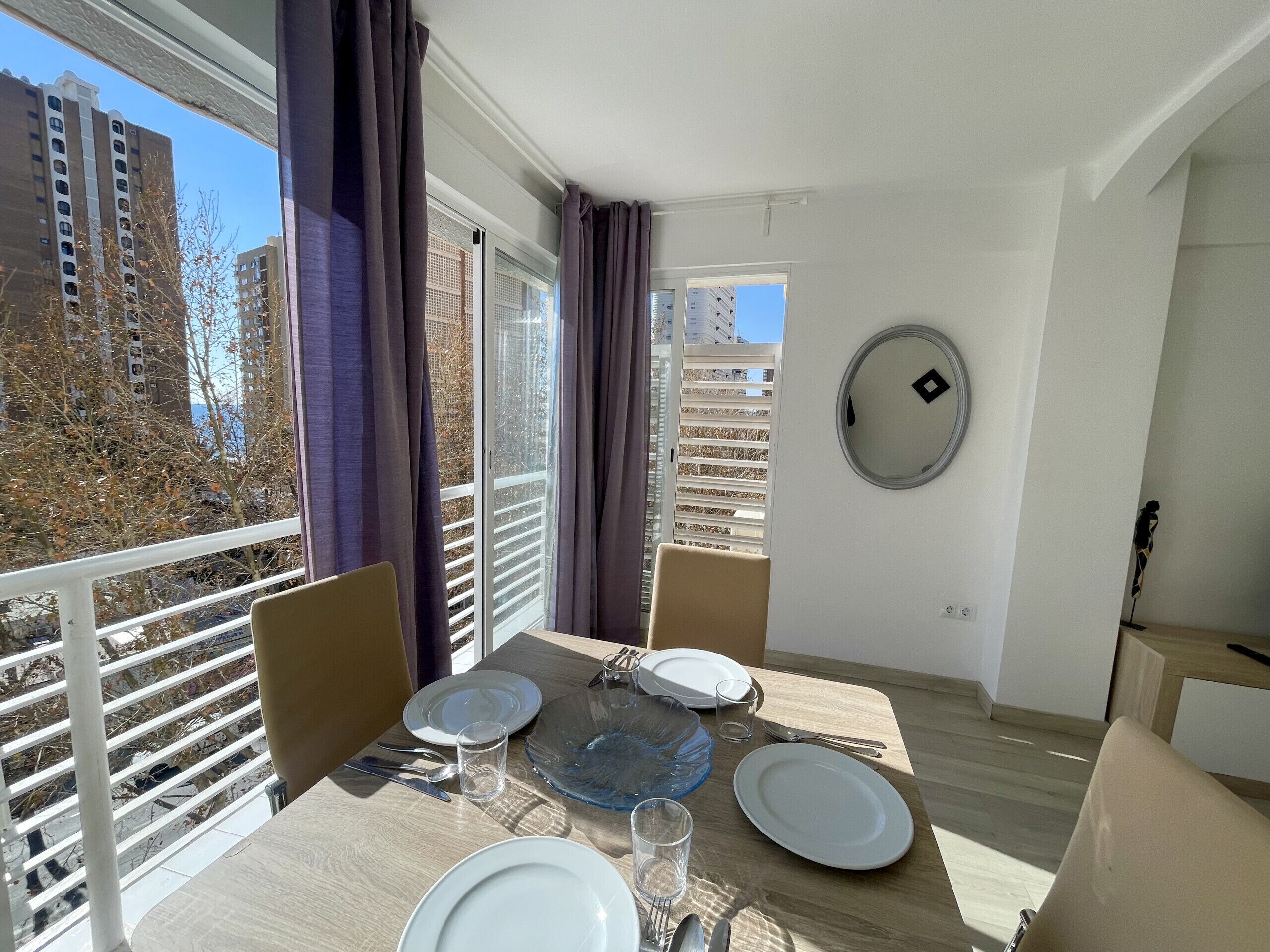 A dining area with a table set for two, a view of the cityscape, and a large window with curtains.