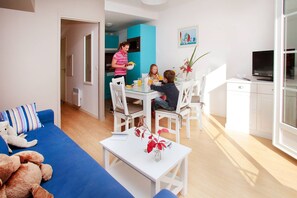 A modern living room with a blue sofa, a dining table with chairs, and a kitchen area with a blue cabinet.