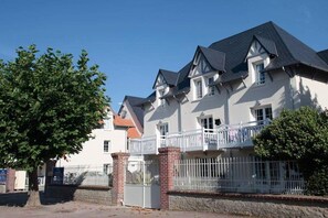 A two-story house with a balcony, a brick chimney, and a white fence.