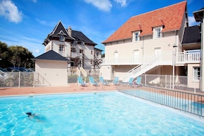 A swimming pool with lounge chairs and a building with a red roof. - Apartment in Cabourg near Beaches (Cabourg)