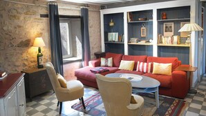 A cozy living room with a red sofa, two armchairs, a coffee table, and a bookshelf filled with books and decorative items. - Cosy Castle with Pool in Onlay (Onlay)