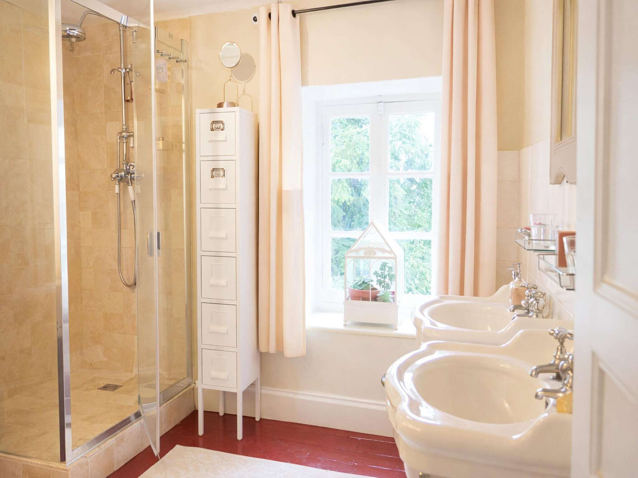 Baño con ducha envuelta en vidrio, tocador con espejo y ventana con vistas a zonas verdes.