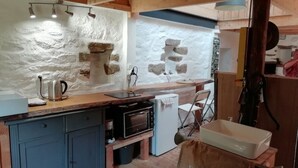 Una cocina rústica con paredes de piedra, vigas de madera, horno empotrado y un lavamanos.